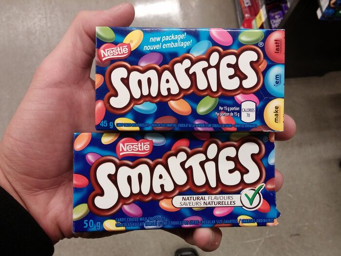 Hand holding two differently sized Smarties candy packages illustrating examples of sneakflation in product packaging.