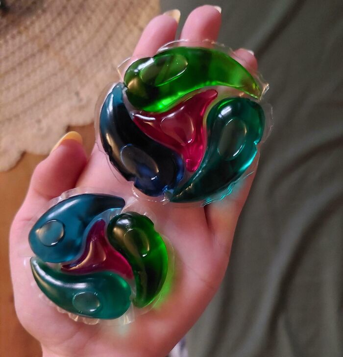 Hand holding two colorful laundry pods of different sizes, illustrating examples of sneakflation in household products.