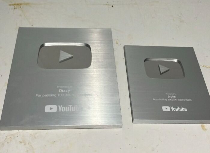 Two silver YouTube play button awards placed side by side on a white surface, showcasing sneakflation in the design.