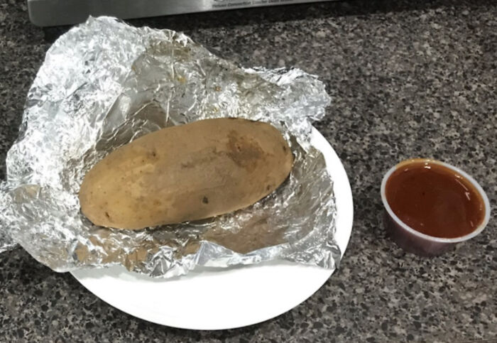 Baked potato wrapped in foil on a plate with a small cup of sauce, illustrating people doing exactly what they were asked to do.