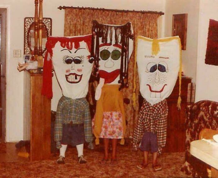 Three people wearing vintage Halloween costumes with large, cartoonish masks and oversized clothes indoors.