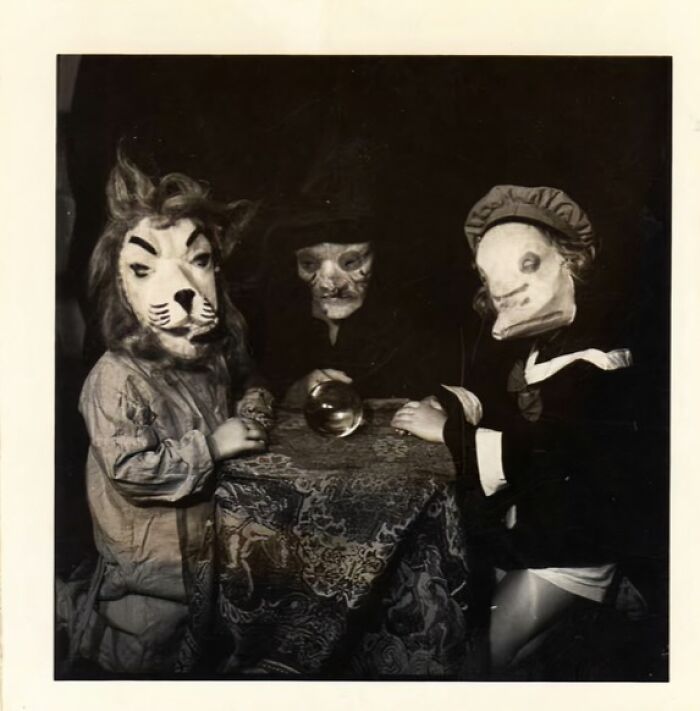 Three children in vintage Halloween costumes with eerie masks gathered around a table with a crystal ball, vintage Halloween costumes.