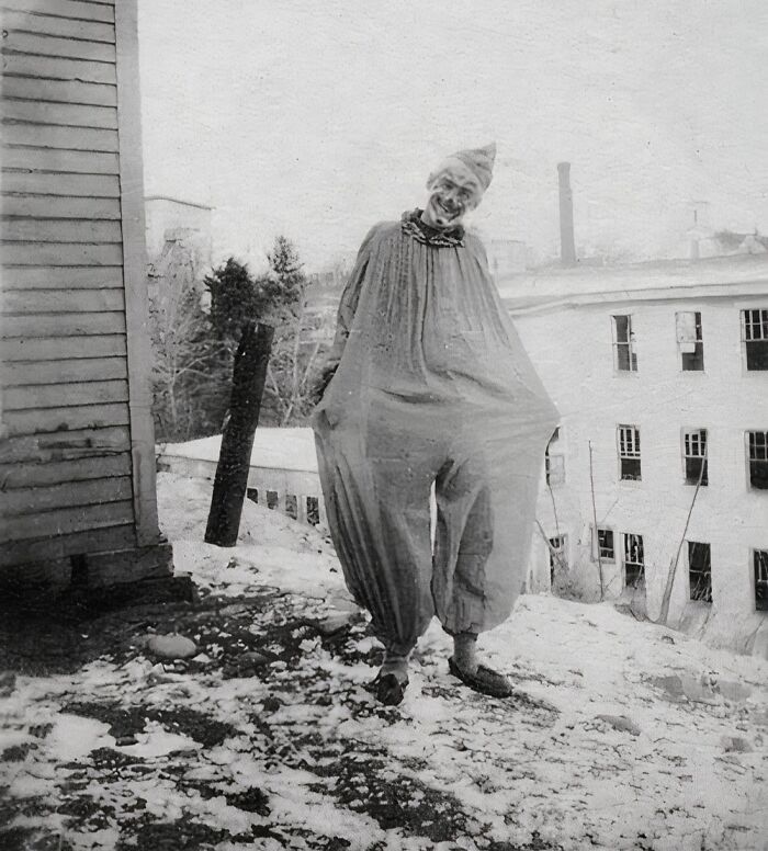 Vintage Halloween costume featuring a frightening clown in an oversized outfit on a snowy outdoor street.