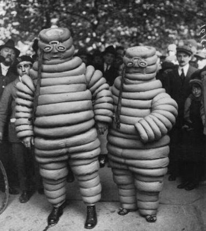 Vintage Halloween costumes featuring two people in segmented, padded suits with creepy masks at a public event.
