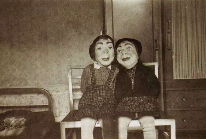 Vintage Halloween costumes featuring eerie character masks and period clothing sitting on a wooden bench in a dimly lit room