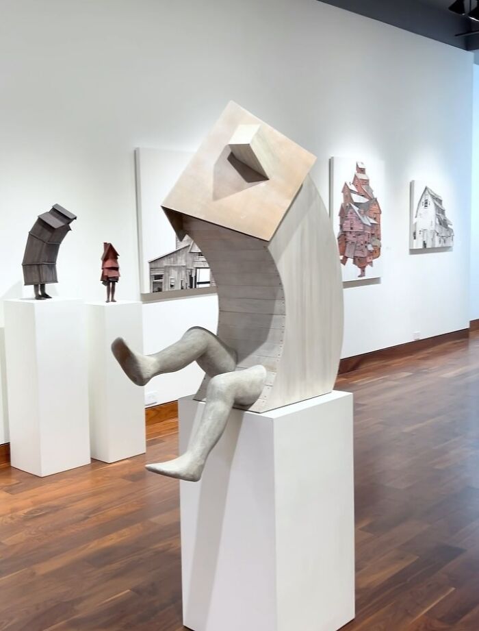Sculpture of surreal walking and collapsing buildings with human legs in a modern art gallery setting.