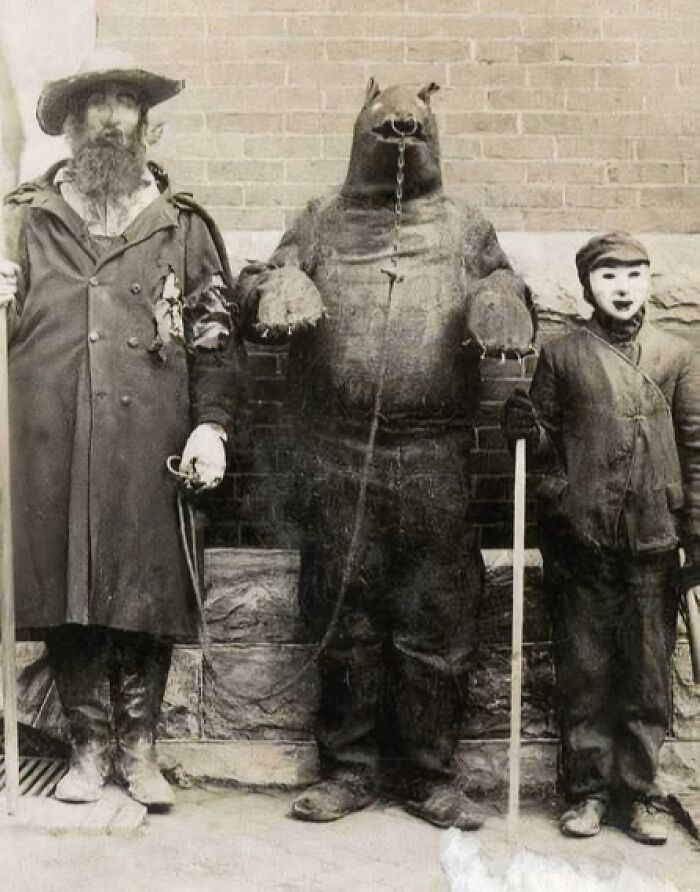 Three people in vintage Halloween costumes including a man, a bear suit, and a child with a mask in old Halloween costumes.