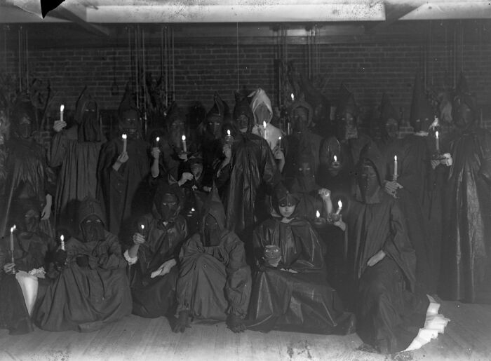 Group of people in dark, hooded Halloween costumes holding candles, showcasing vintage terrifying and impressive Halloween costumes.