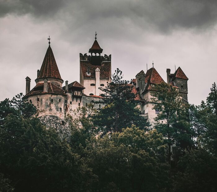 Spooky castle with red rooftops surrounded by dark forest under a gloomy sky, a top spooky destination for Halloween visitors.