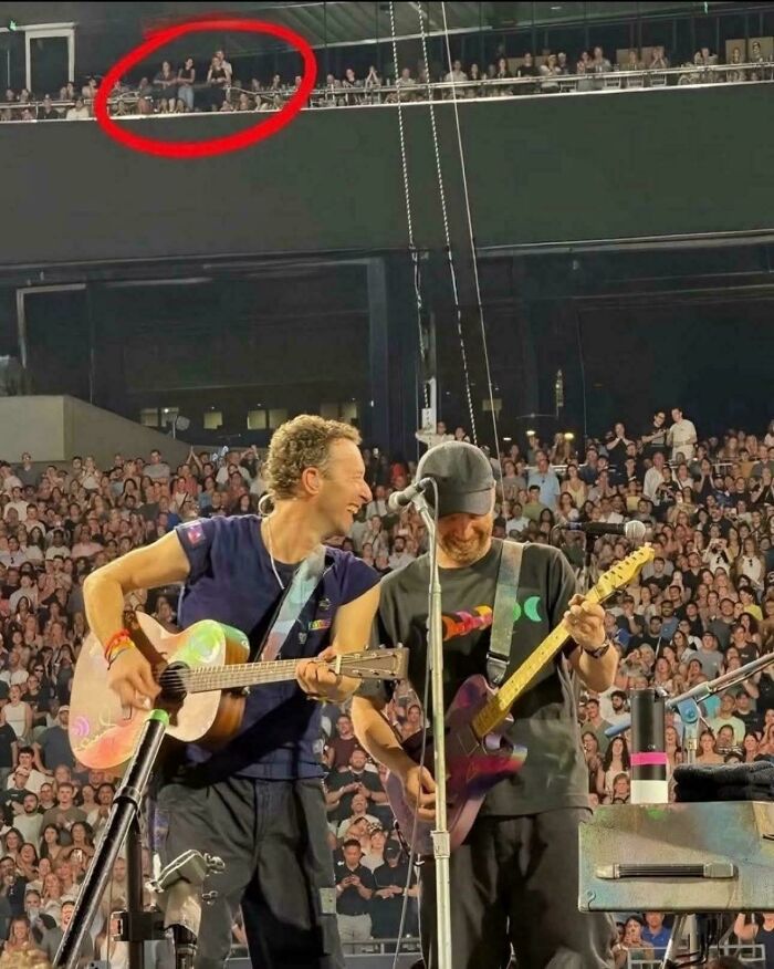 Two musicians playing guitars on stage at a concert with a crowd and a red circle highlighting people above before disaster struck.