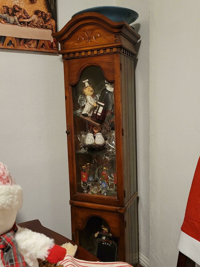 Wooden display cabinet with glassware and chef figurines teetering before disaster in a hilarious photo moment.