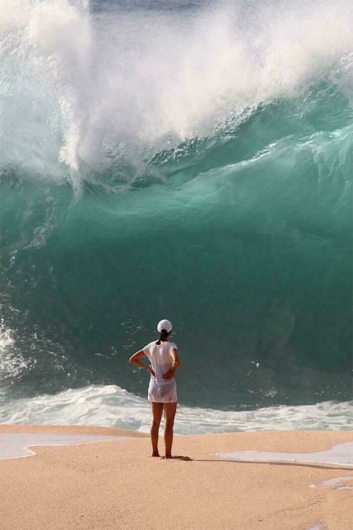 Person standing on the beach facing a huge ocean wave, a hilarious photo taken before disaster struck.