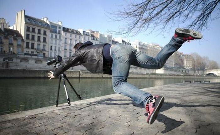 Person falling while taking a photo with camera and tripod by the riverside, a hilarious photo before disaster struck.