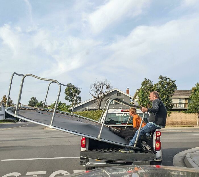 Man and boy holding a large trampoline in a truck bed before a likely hilarious disaster struck in a suburban neighborhood.