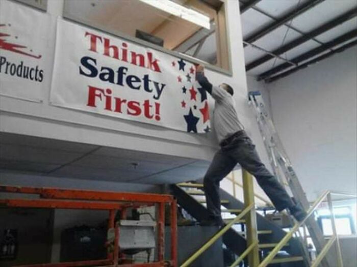 Man dangerously balancing on railing while hanging a safety banner, a hilarious photo taken before disaster struck.