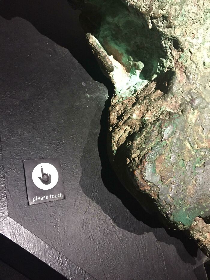 Sign saying please touch next to a corroded metal object, illustrating unhinged pics of people doing exactly what they were asked to do.