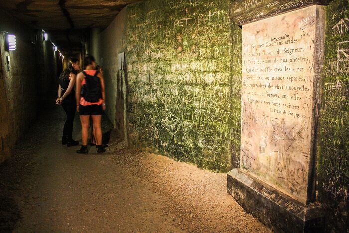 Two people exploring a dimly lit underground tunnel covered in graffiti at a spooky destination for Halloween visitors.