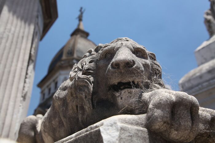 Stone lion statue with historic building in the background at a spooky destination perfect for Halloween visits.