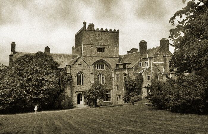 Vintage photo of a spooky haunted mansion surrounded by trees and lawn, a top spooky destination for Halloween visits.