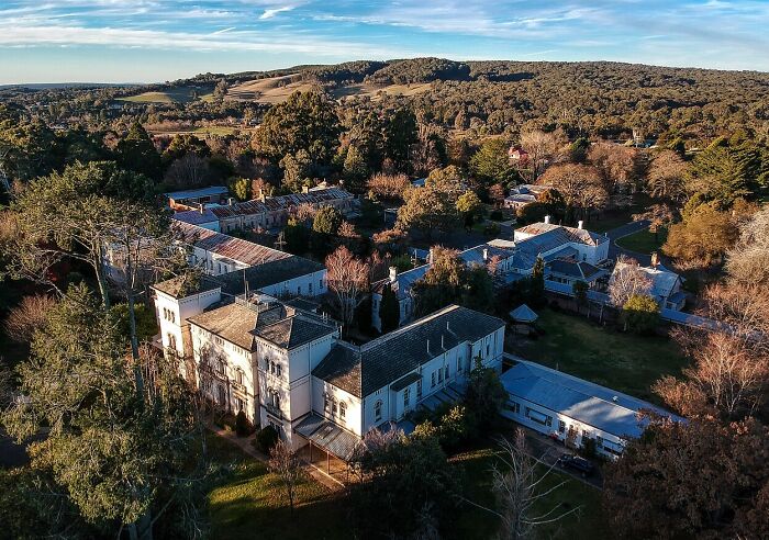 Aerial view of an old, eerie mansion surrounded by dense trees and a gloomy landscape, a spooky destination for Halloween.