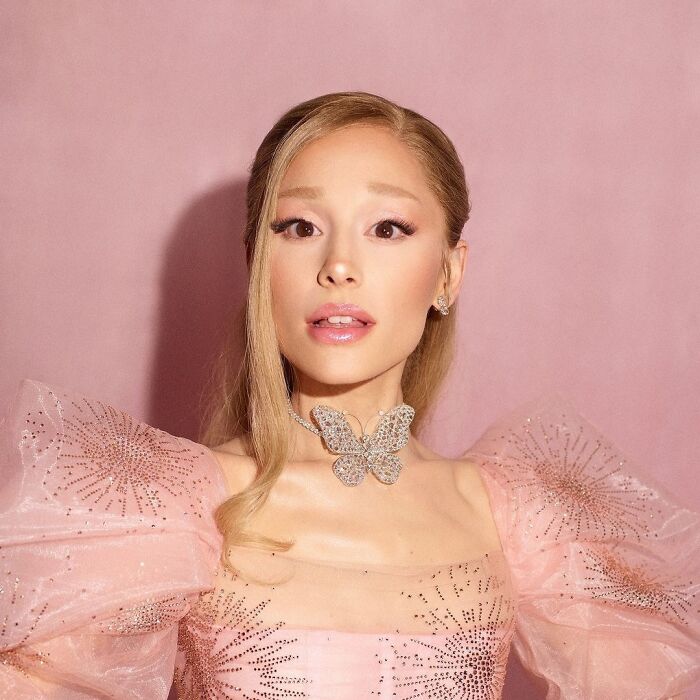 Young woman in a pink dress with a butterfly necklace, representing 2024 pop culture moments that caught viewers off guard.