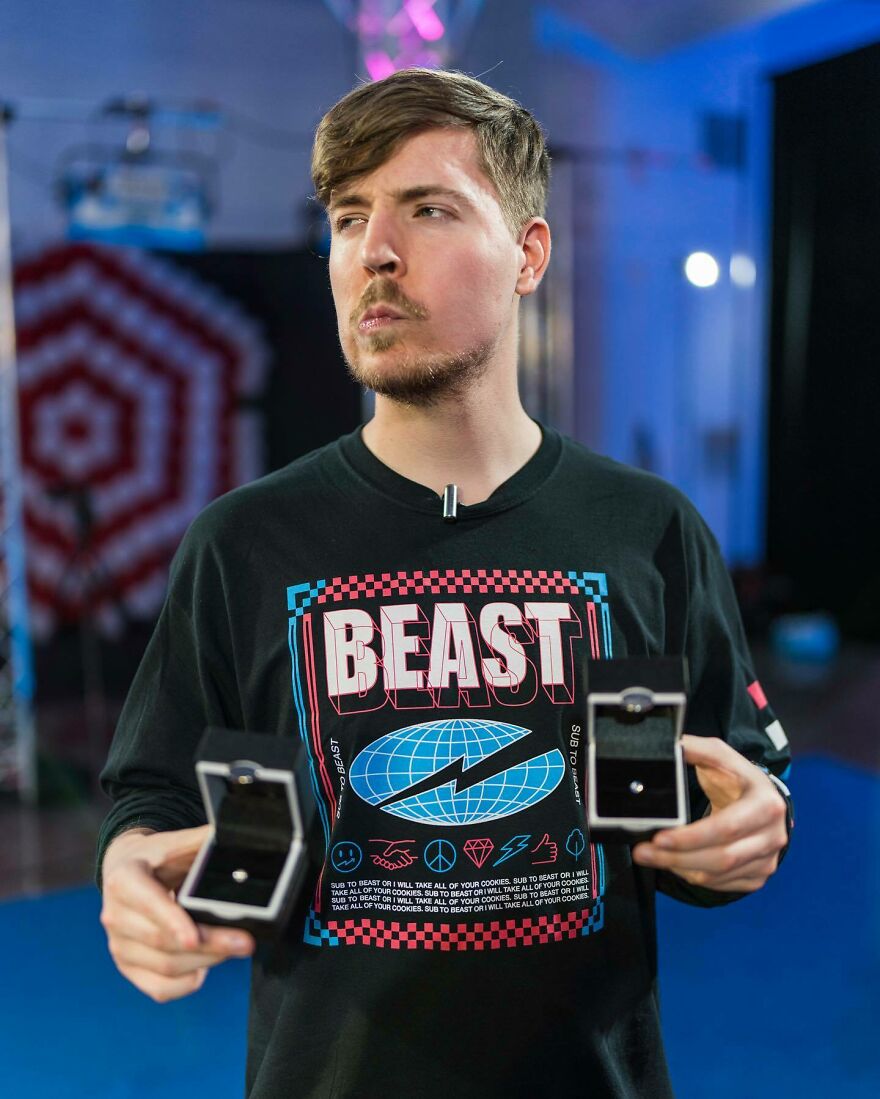 Young man wearing a Beast shirt holding two open ring boxes in a studio setting for 2024 pop culture moments shock.