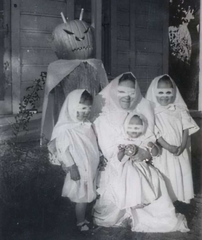 Black and white photo of children and adult in ghost costumes with a large pumpkin head figure, vintage Halloween costumes.