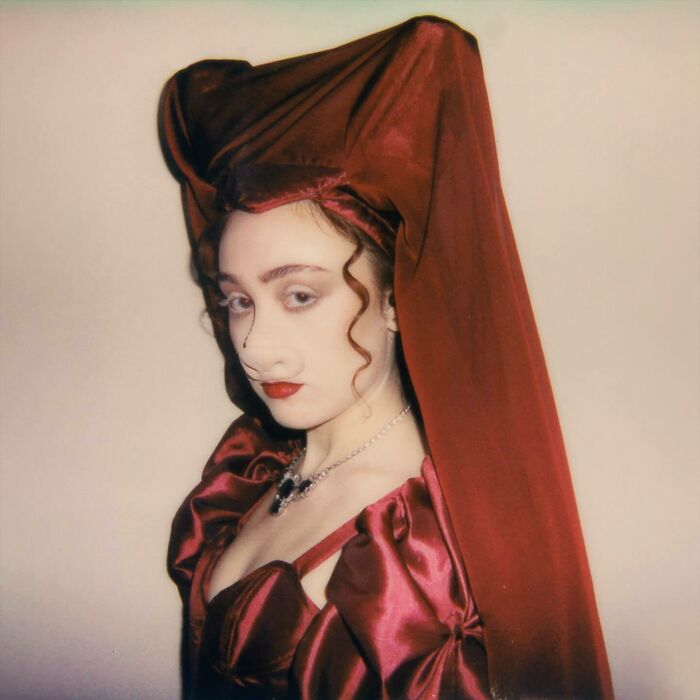 Person in elaborate red satin outfit and headpiece, styled with vintage curls, representing 2024 pop culture moments that caught off guard.