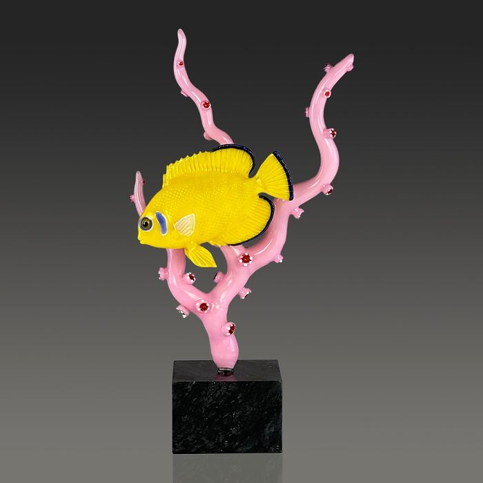 Yellow glass fish sculpture mounted on pink coral glass stand, showcasing stunning glass sculptures inspired by ocean life.