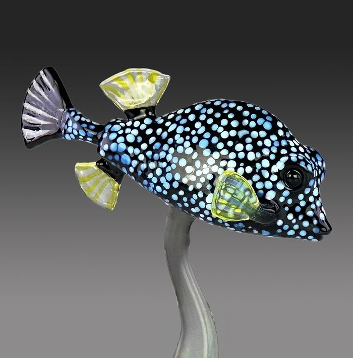 Glass sculpture of a spotted fish with blue and yellow fins, showcasing stunning ocean life inspired artwork.