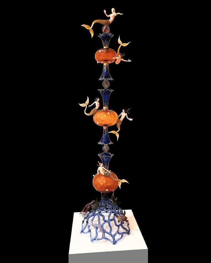 Tall glass sculpture featuring mermaids and ocean elements, showcasing stunning glass sculptures inspired by ocean life.