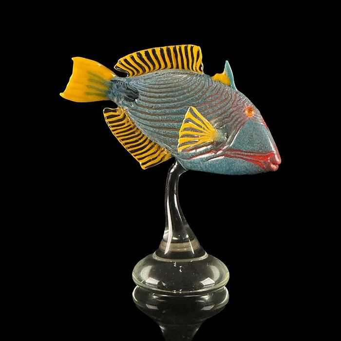 Glass sculpture of a colorful tropical fish with yellow striped fins, showcasing stunning ocean life artistry on a clear stand.