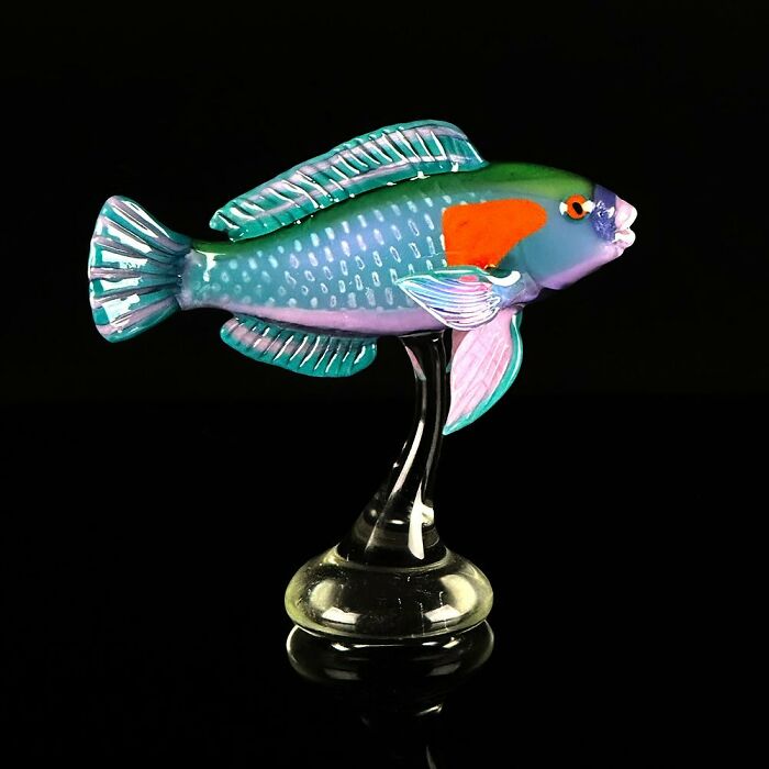 Colorful glass sculpture of a fish showcasing stunning ocean life in vivid detail on a clear glass stand against black background