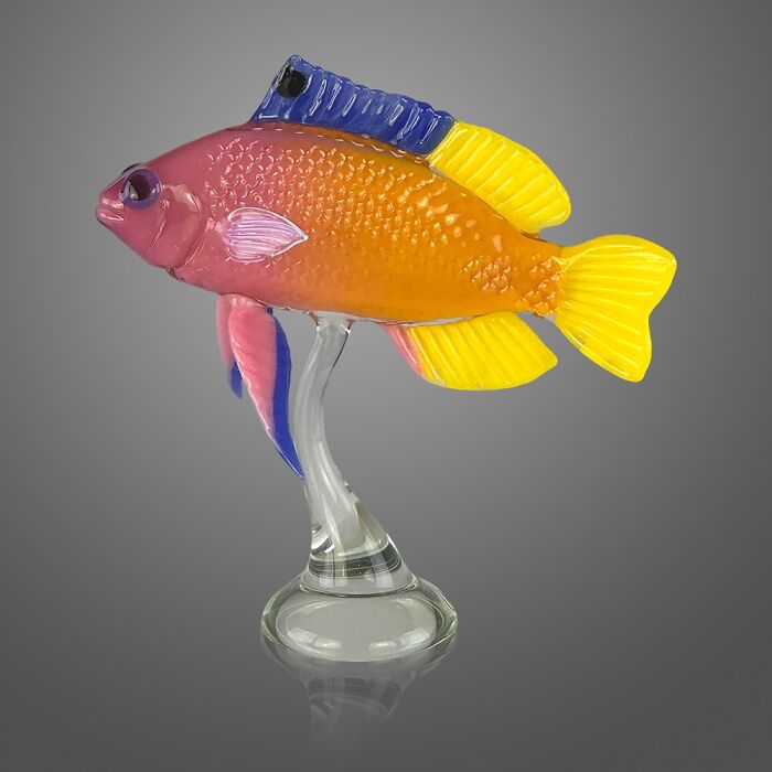 Colorful glass sculpture of a fish showcasing stunning ocean life details on a clear glass base against a gray background.