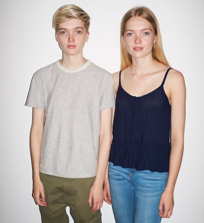 Young celebrity twins standing side by side, one with short blonde hair wearing a gray shirt, and the other with long hair in a black top.