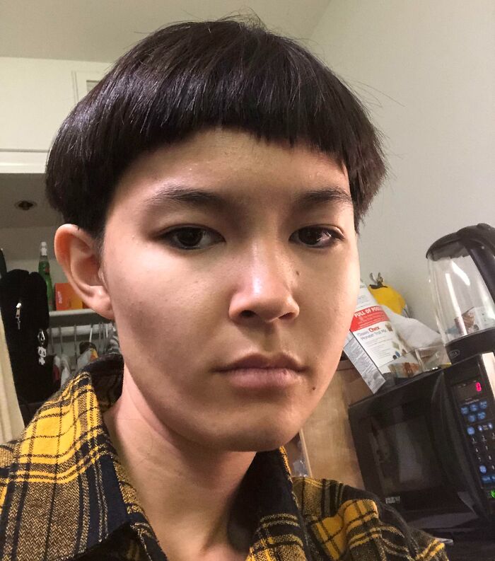 Person with a tragic hair accident haircut wearing a yellow plaid shirt indoors, looking at the camera with a neutral expression.