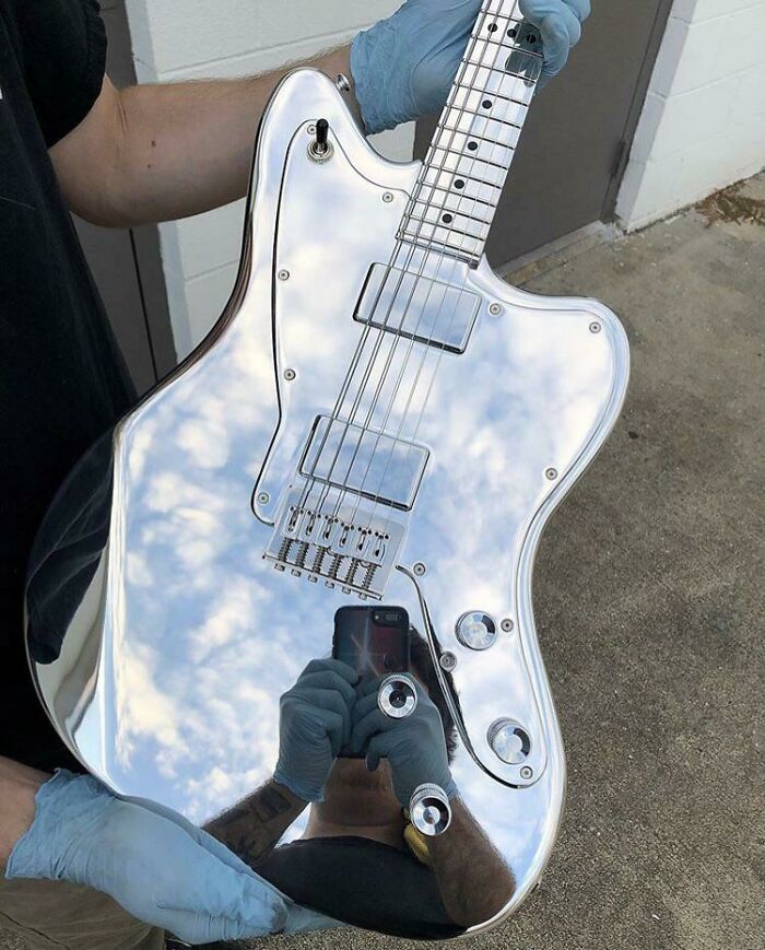 Electric guitar with a mirror-like reflective surface showing sky clouds and person taking a photo, highlighting reflection selling it.