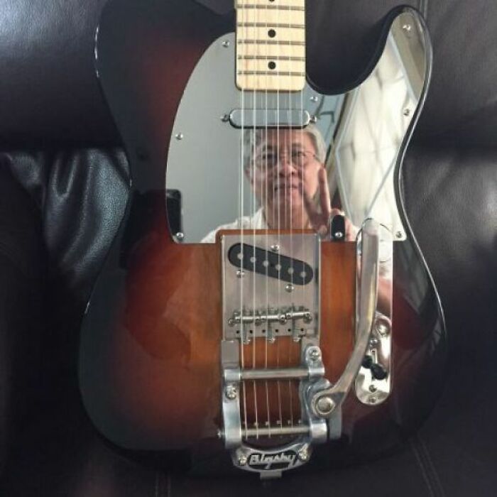 Electric guitar with a mirror reflection showing a person making a peace sign, highlighting hilarious mirror sales moments.
