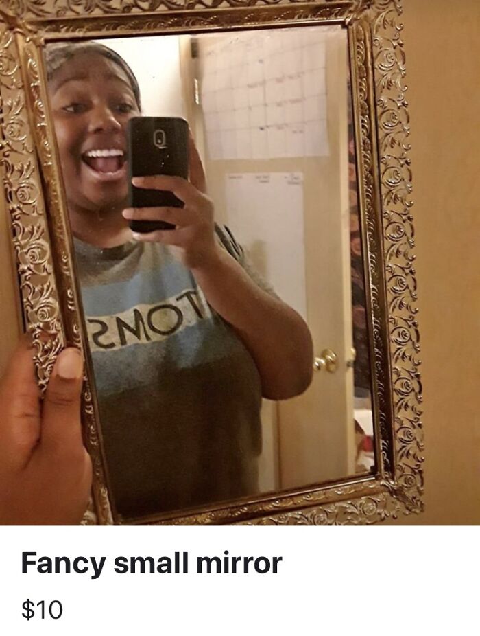 Person holding a fancy small mirror with an ornate frame showing a smiling selfie reflection.