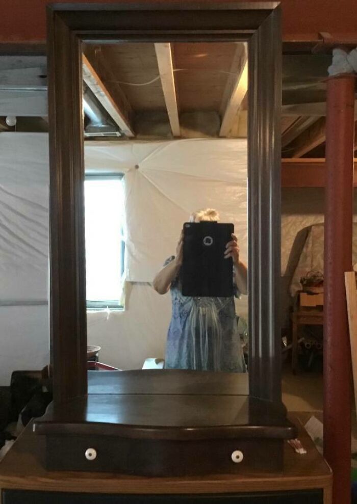 Person using a tablet to take a photo of a mirror for sale, highlighting the reflection in the basement setting.