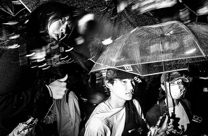 Black and white street photograph capturing the beauty of everyday life in India with people under an umbrella in the rain.