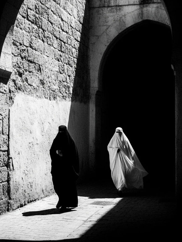 Black and white street photography capturing two women in contrasting veils walking under an archway in everyday life in India.