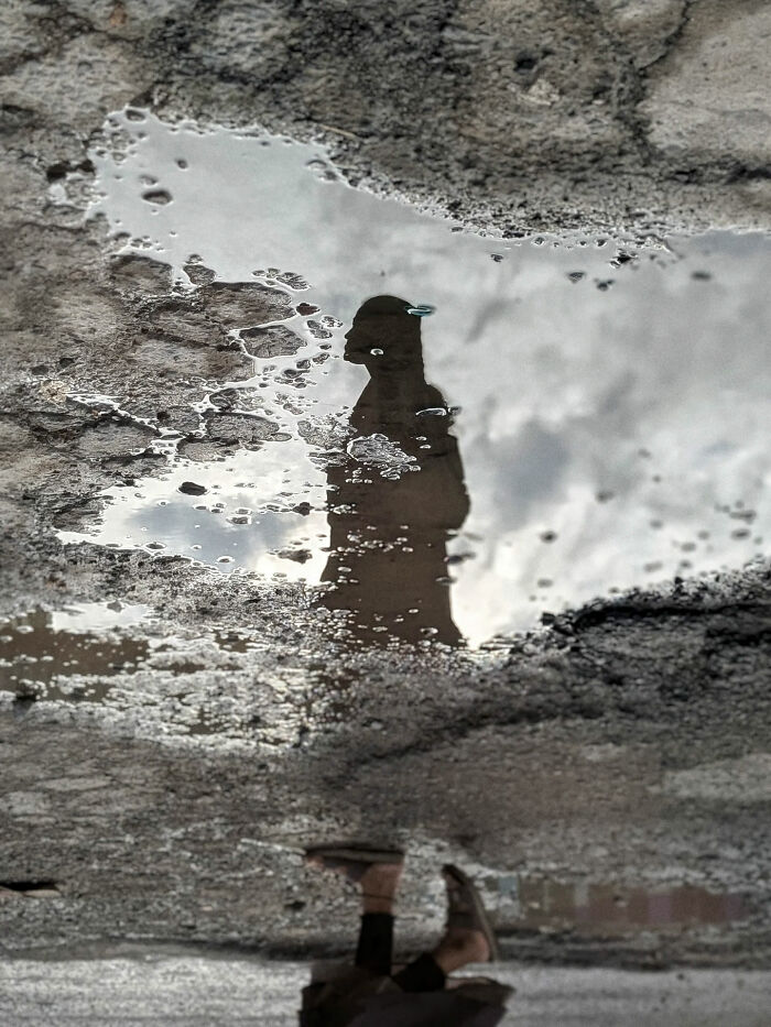Reflection of a person in a puddle on a rough street, capturing everyday life in India by street photographer.