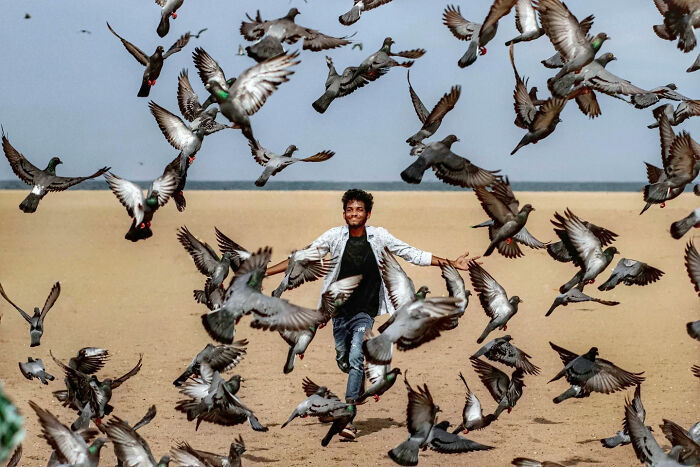 Young man joyfully running on a beach surrounded by flying pigeons, capturing the beauty of everyday life in India.