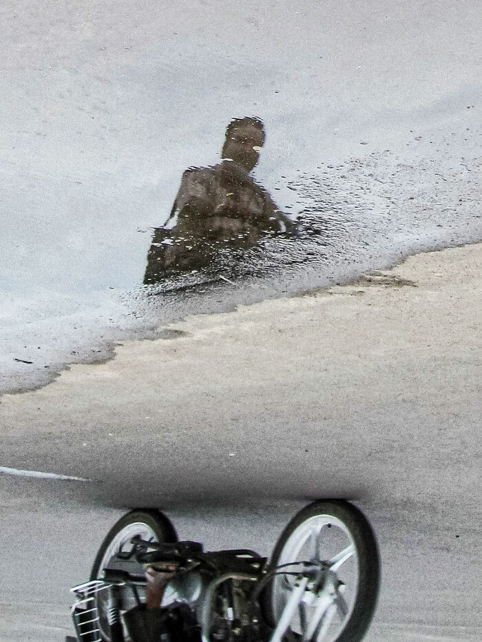Reflection of a man riding a bicycle on wet street, capturing the beauty of everyday life in India by street photographer.