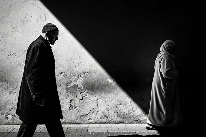 Black and white street photograph capturing the beauty of everyday life in India with two people walking past a textured wall.