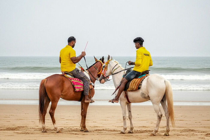 Two men in yellow shirts riding horses on an Indian beach, capturing the beauty of everyday life in India by street photography.