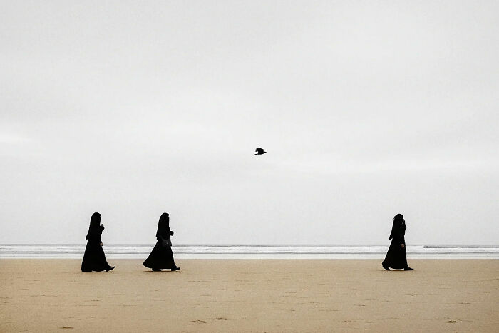 Three women in black walking on a beach with a bird flying above, capturing the beauty of everyday life in India.