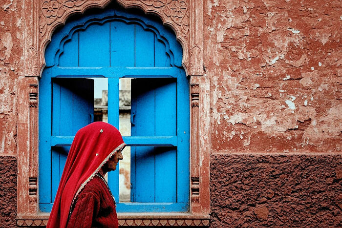 Woman in traditional attire walking past a vibrant blue window, capturing the beauty of everyday life in India by street photography