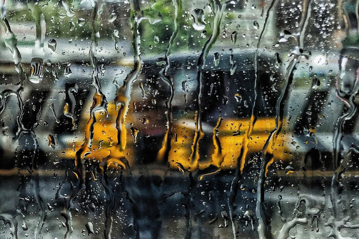 Yellow auto rickshaw seen through rain-covered window, capturing the beauty of everyday life in India by a street photographer.